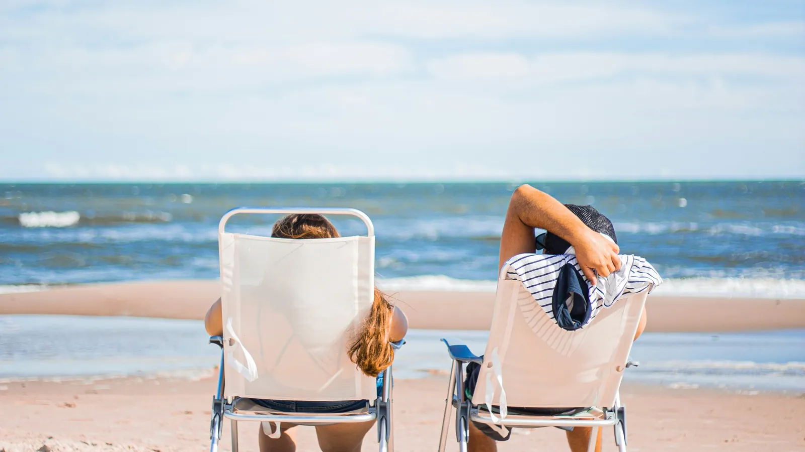 A couple relaxing in beach chairs looking out at the ocean on a sunny summer day